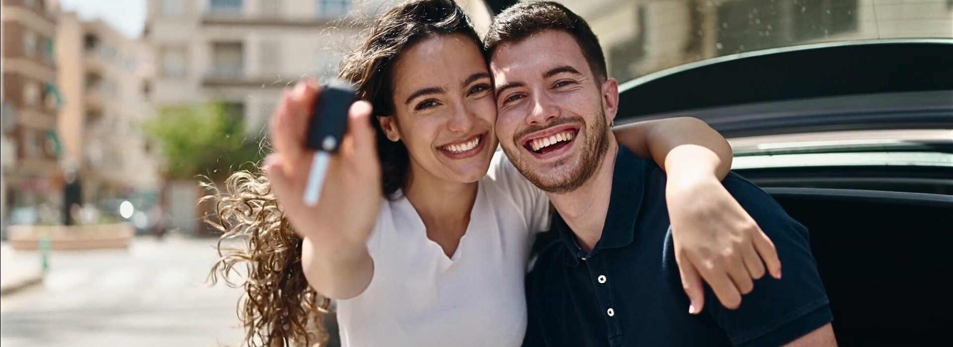 A happy Caucasian couple waving car keys from their new car in the air.